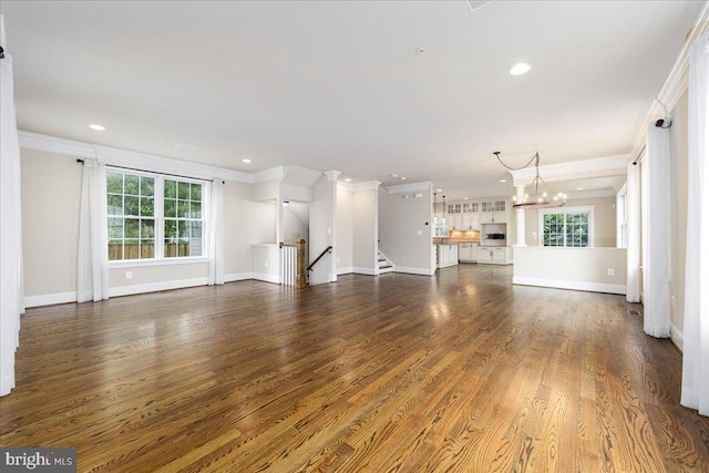 unfurnished living room featuring crown molding, a notable chandelier, wood finished floors, and a healthy amount of sunlight