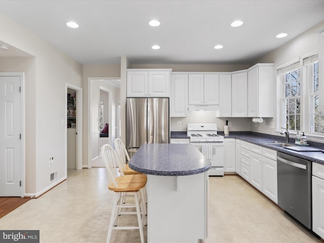 kitchen featuring visible vents, a sink, stainless steel appliances, white cabinets, and dark countertops