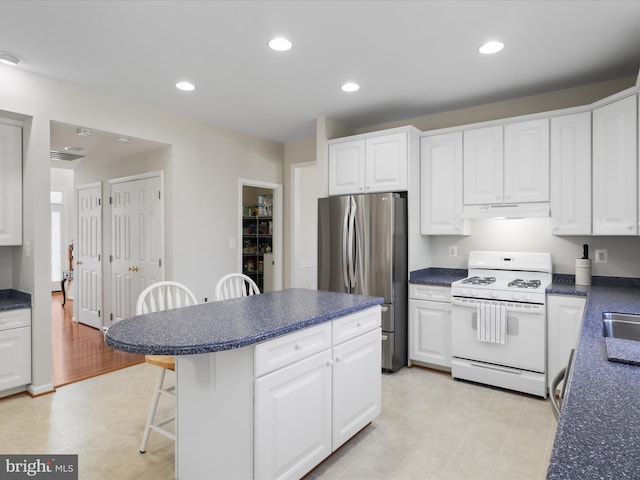 kitchen featuring a breakfast bar area, freestanding refrigerator, white gas range oven, under cabinet range hood, and dark countertops