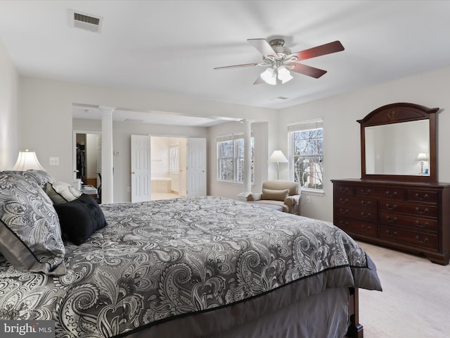 carpeted bedroom featuring ensuite bath, decorative columns, visible vents, and ceiling fan