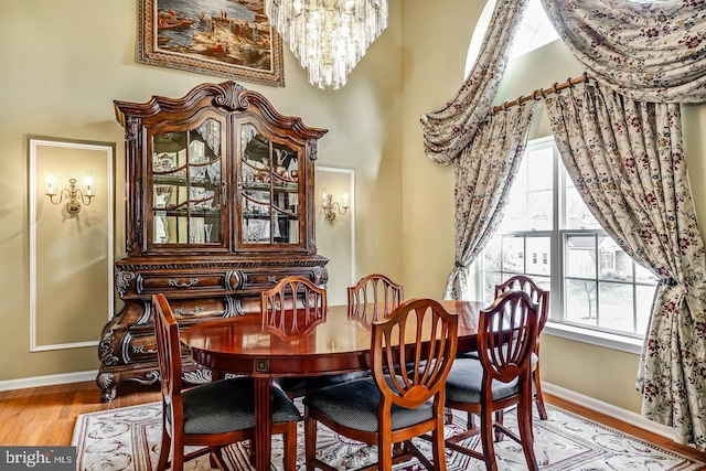 dining room featuring light wood-style floors, a high ceiling, a notable chandelier, and baseboards