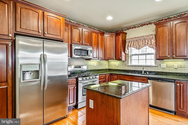 kitchen with stainless steel appliances, backsplash, a sink, and light wood-style flooring