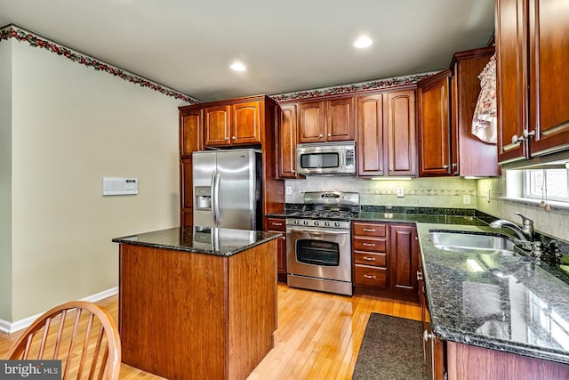 kitchen with stainless steel appliances, a sink, light wood finished floors, a center island, and tasteful backsplash