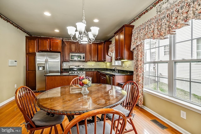 kitchen with tasteful backsplash, dark countertops, appliances with stainless steel finishes, light wood-style floors, and a chandelier