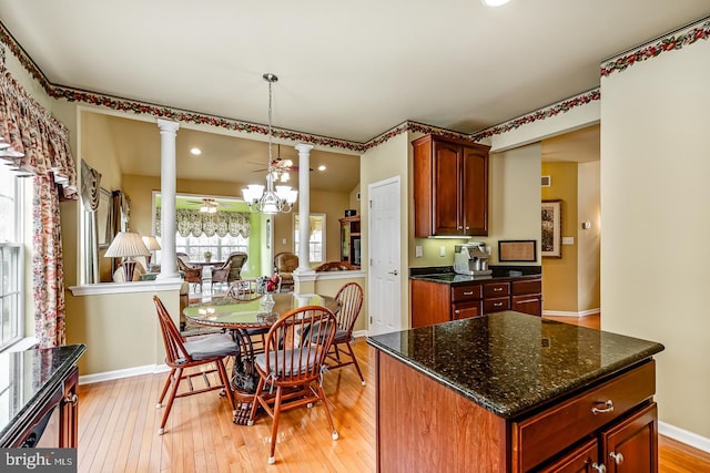 kitchen with decorative columns, baseboards, dark stone counters, a ceiling fan, and light wood-style floors