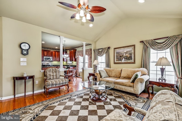 living room with baseboards, a ceiling fan, wood finished floors, vaulted ceiling, and ornate columns