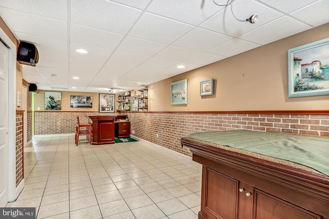 interior space with light tile patterned floors, brick wall, a bar, and wainscoting