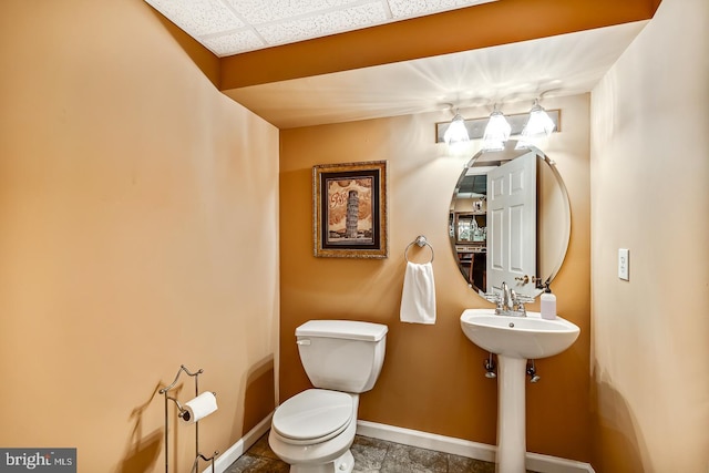 half bath with a paneled ceiling, baseboards, and toilet