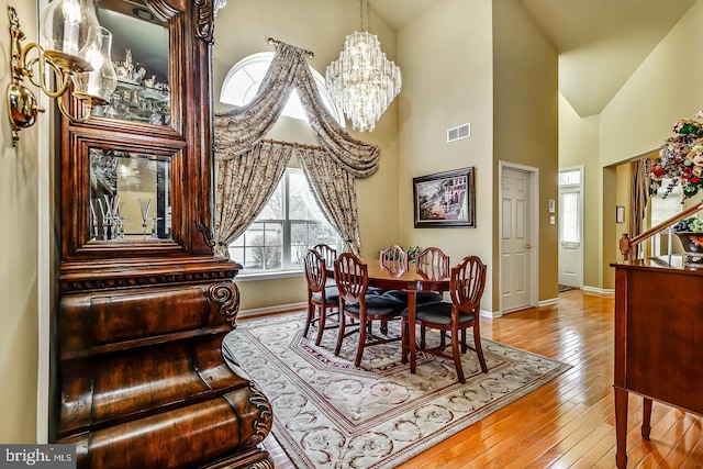 dining room featuring a chandelier, high vaulted ceiling, hardwood / wood-style flooring, visible vents, and baseboards