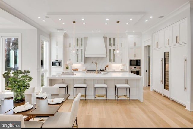 kitchen with oven, built in microwave, light wood-type flooring, premium range hood, and white cabinetry