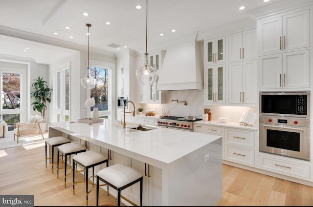 kitchen with light wood-style flooring, custom exhaust hood, stainless steel appliances, white cabinetry, and a sink