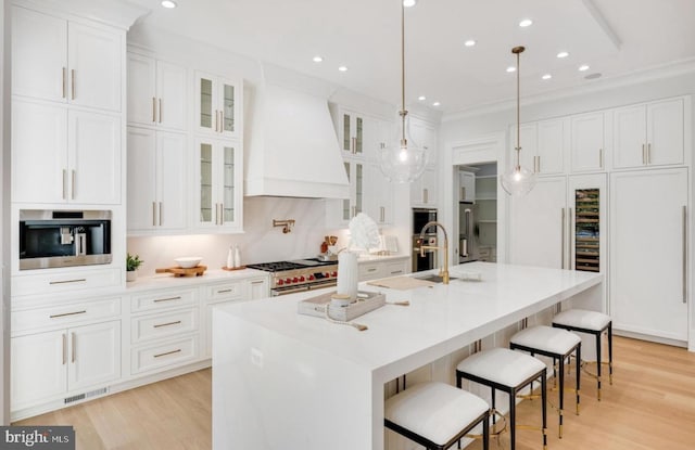 kitchen featuring premium appliances, white cabinets, premium range hood, and a center island with sink