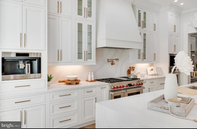 kitchen with range with two ovens, light countertops, custom range hood, glass insert cabinets, and white cabinets