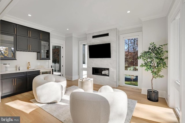 living room with light wood-type flooring, recessed lighting, ornamental molding, and a high end fireplace