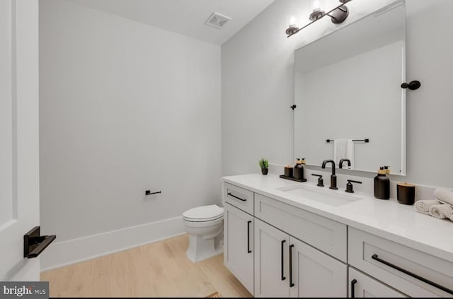 bathroom with visible vents, toilet, vanity, wood finished floors, and baseboards