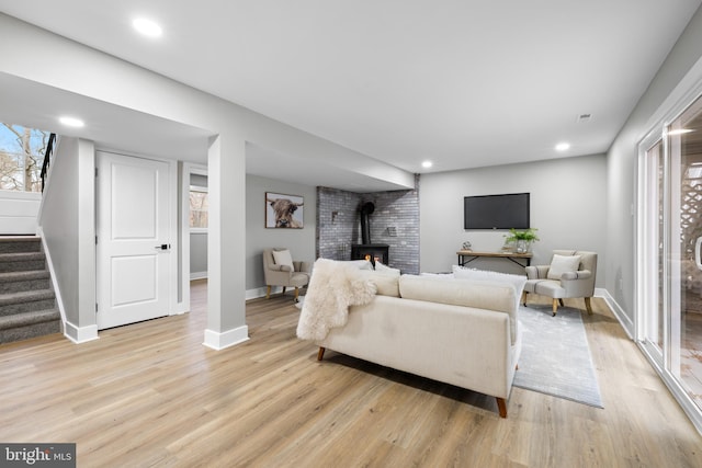 living room with light wood-style floors, a wood stove, baseboards, and stairs