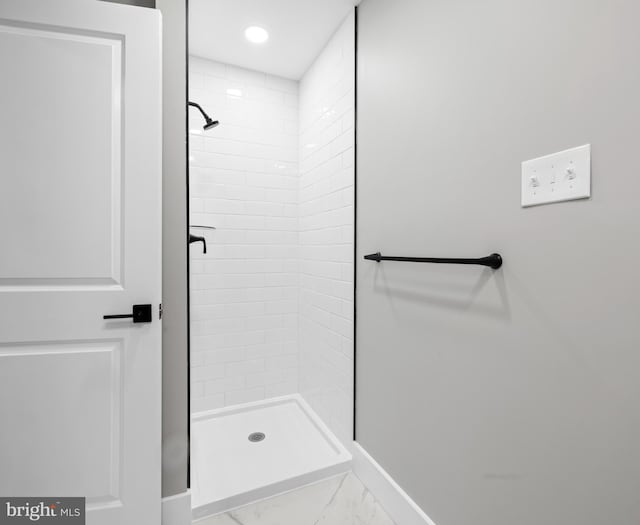 bathroom featuring marble finish floor, a shower stall, and baseboards