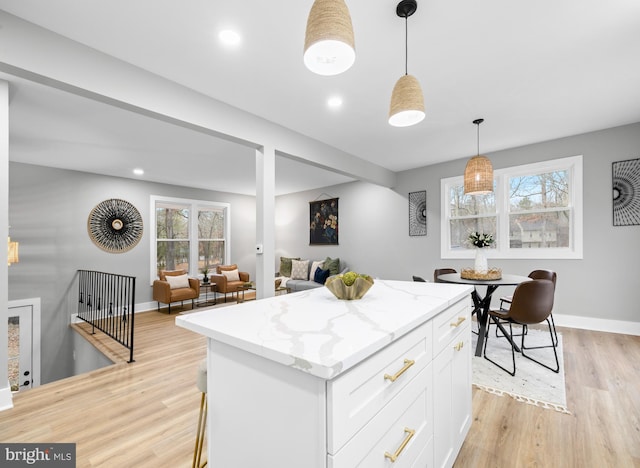 kitchen featuring white cabinets, a center island, hanging light fixtures, light stone countertops, and light wood-style floors