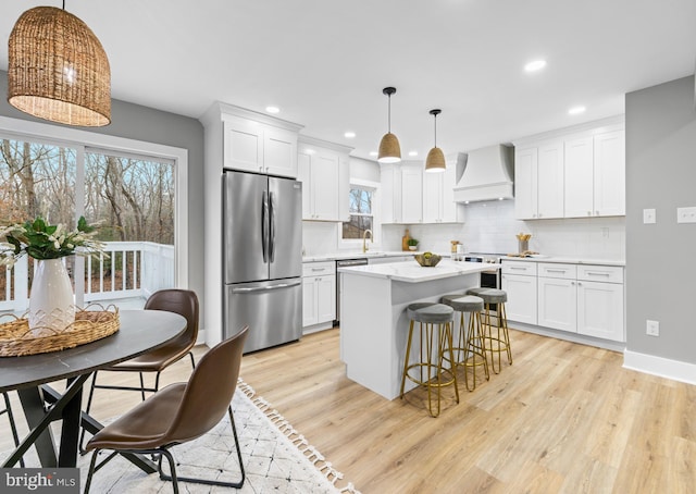 kitchen with light wood-style flooring, a sink, appliances with stainless steel finishes, decorative backsplash, and custom range hood