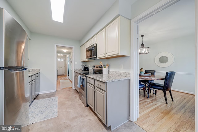 kitchen featuring light stone counters, baseboards, light wood-style flooring, gray cabinetry, and appliances with stainless steel finishes