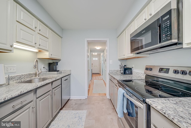 kitchen featuring baseboards, light stone countertops, white cabinets, stainless steel appliances, and a sink