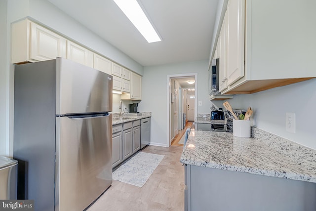 kitchen with baseboards, light wood-type flooring, light stone counters, stainless steel appliances, and a sink