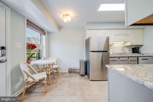 kitchen with light stone counters, a sink, appliances with stainless steel finishes, white cabinets, and baseboards