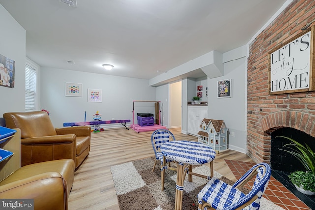 living area featuring visible vents, baseboards, a brick fireplace, and wood finished floors