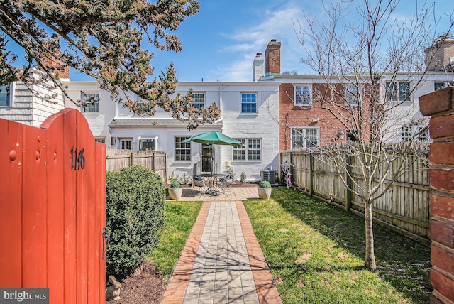 rear view of house with a patio, brick siding, a fenced backyard, and a chimney