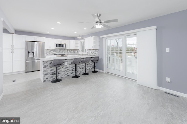 kitchen with backsplash, white cabinetry, stainless steel appliances, a peninsula, and a breakfast bar area