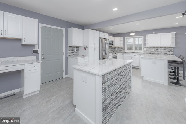 kitchen with a breakfast bar, open shelves, white cabinetry, appliances with stainless steel finishes, and light stone countertops