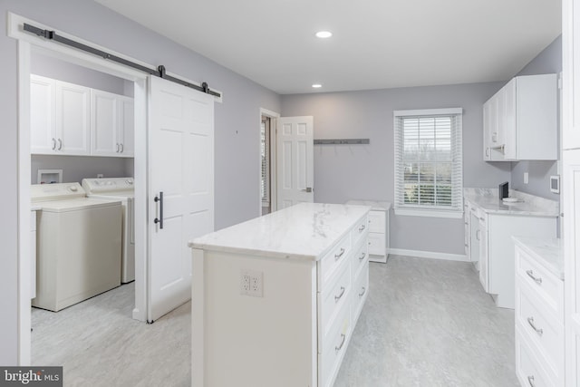 kitchen featuring light stone countertops, white cabinets, a center island, and washing machine and clothes dryer