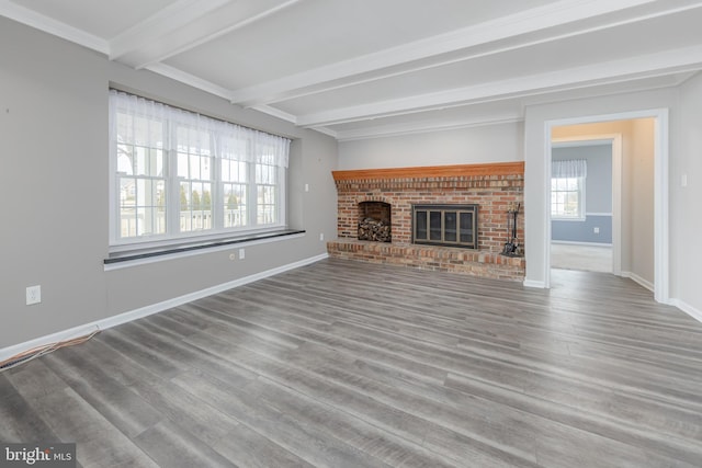 unfurnished living room featuring beam ceiling, a brick fireplace, baseboards, and wood finished floors