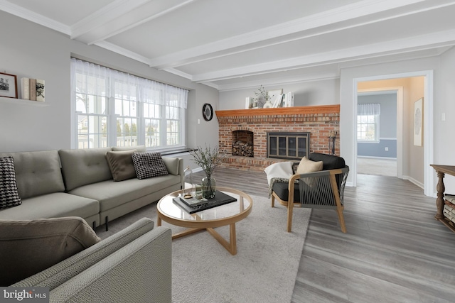 living room featuring wood finished floors, baseboards, beam ceiling, crown molding, and a brick fireplace