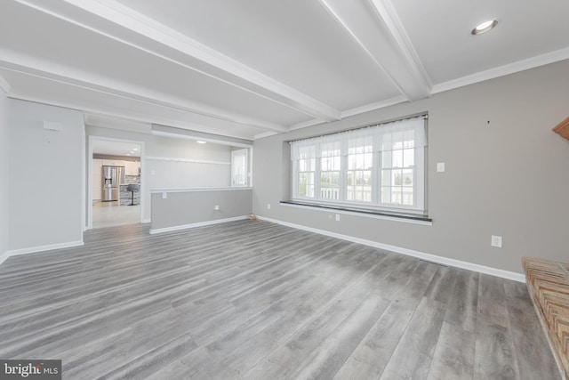 unfurnished living room featuring beamed ceiling, baseboards, and wood finished floors