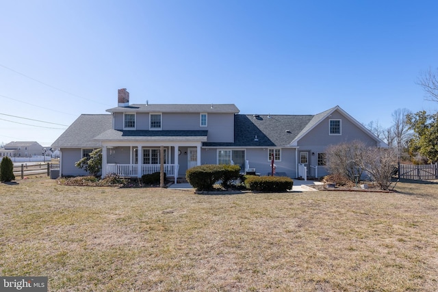 rear view of property featuring a porch, fence, a lawn, and a chimney