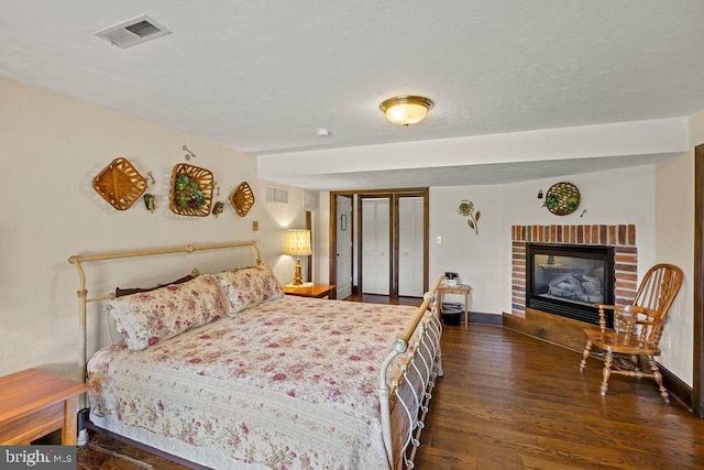 bedroom featuring baseboards, visible vents, wood finished floors, a textured ceiling, and a brick fireplace