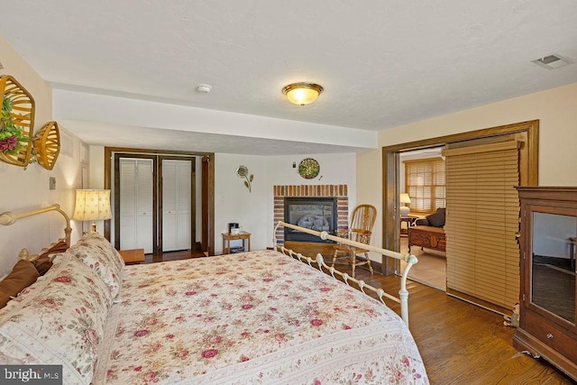 bedroom with a textured ceiling, a fireplace, wood finished floors, visible vents, and a closet