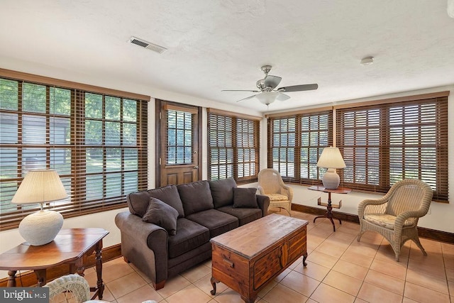 living room with light tile patterned floors, ceiling fan, a textured ceiling, visible vents, and baseboards