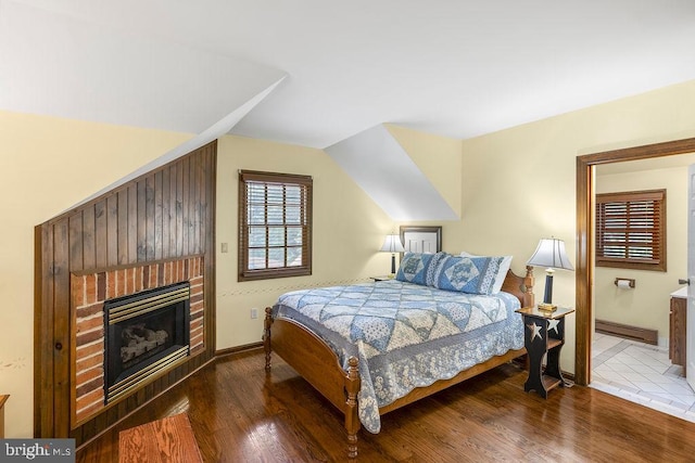 bedroom featuring baseboards, wood finished floors, vaulted ceiling, a brick fireplace, and a baseboard heating unit