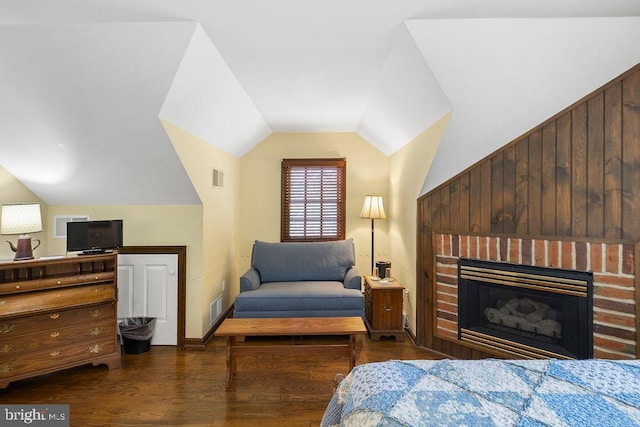 bedroom with lofted ceiling, visible vents, a fireplace, and wood finished floors