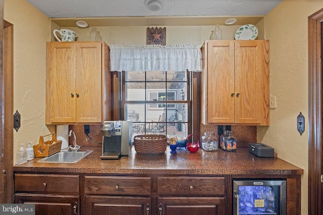 kitchen with a textured wall, wine cooler, dark countertops, and a sink