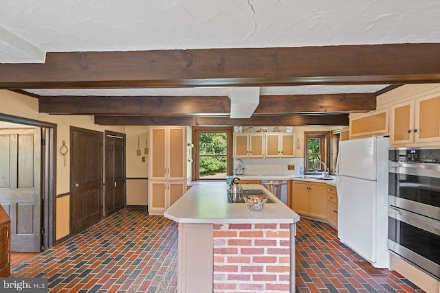 kitchen with brick floor, a sink, light countertops, appliances with stainless steel finishes, and beamed ceiling