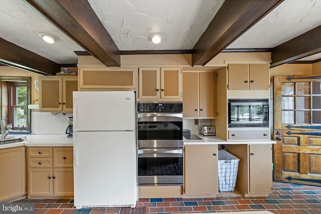 kitchen featuring brick floor, a sink, light countertops, appliances with stainless steel finishes, and beamed ceiling