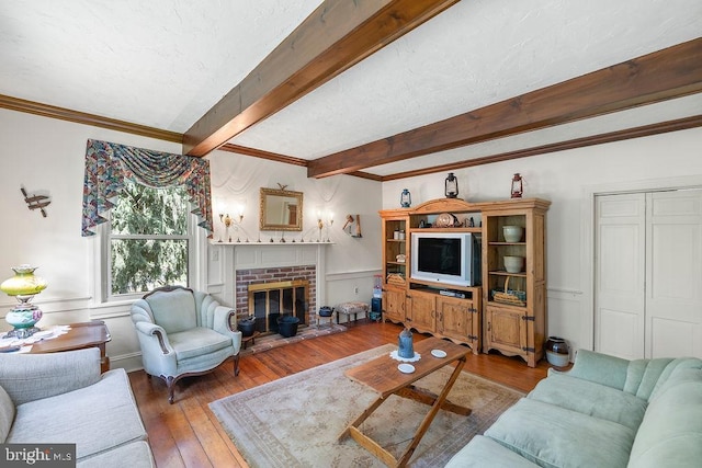 living room featuring a fireplace, a decorative wall, ornamental molding, beamed ceiling, and hardwood / wood-style flooring