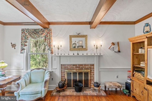 living room with crown molding, beam ceiling, a fireplace, and wood finished floors