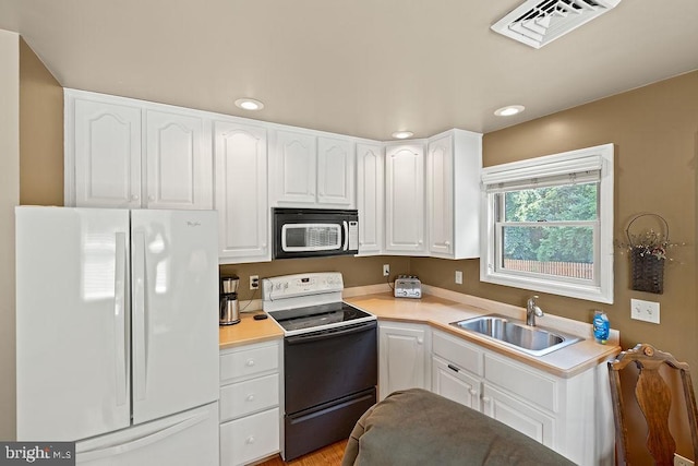 kitchen with a sink, visible vents, white cabinets, electric stove, and freestanding refrigerator