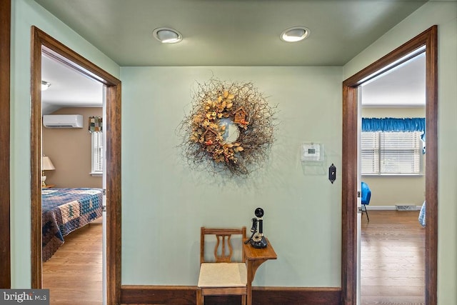 hallway featuring wood finished floors, visible vents, baseboards, and a wall mounted AC