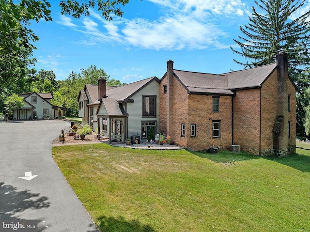 view of front of home featuring central air condition unit, a chimney, a front lawn, and brick siding