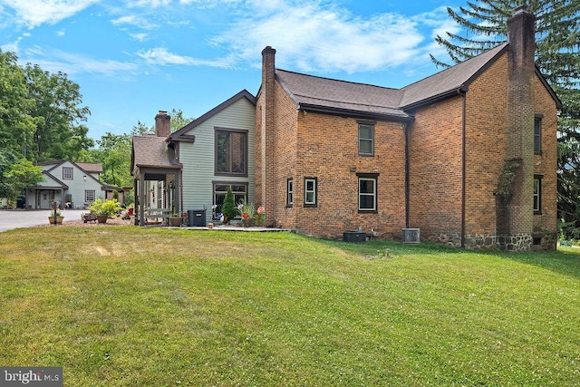 back of property with brick siding, a chimney, central AC, and a yard